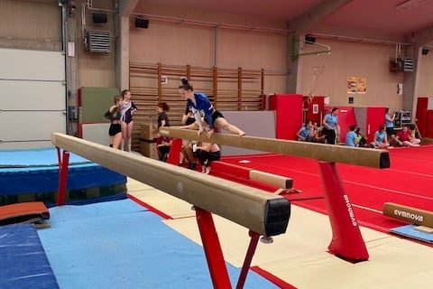 Une élève faisant le grand écart sur une poutre dans une salle de gymnastique